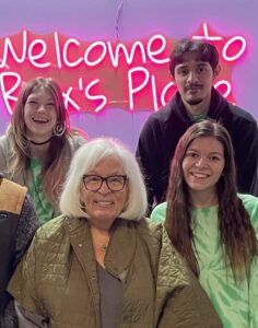 Kathy in front of entry sign surrounded by Kree, Luis and Chloe